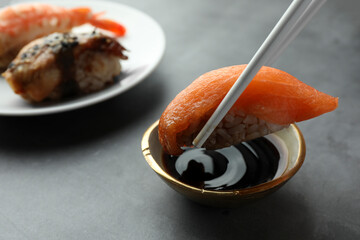 Dipping tasty nigiri sushi with salmon into soy sauce on grey table, closeup