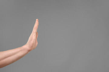 Man showing stop gesture on grey background, closeup. Space for text