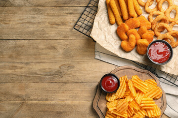 Tasty ketchup and different snacks on wooden table, flat lay. Space for text