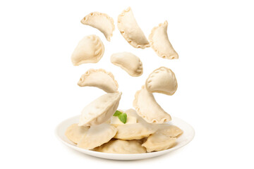 Many raw dumplings (varenyky) falling onto plate with cooked ones against white background