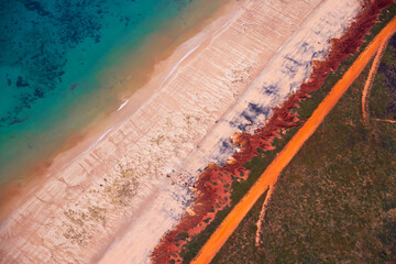 Aerial view of red sandy coastline and dirt track along turquoise water at Dampier Peninsula,...