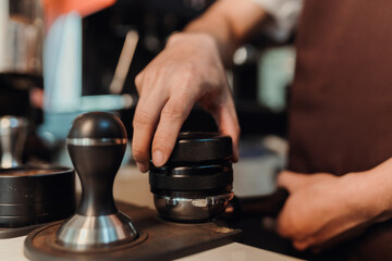 Closeup hand of barista preparation tampering ground coffee in portafilter for espresso machine. Coffee making concept.
