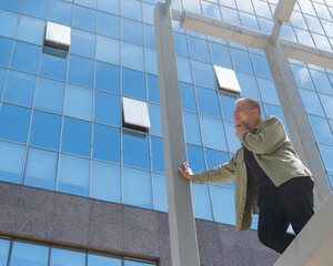 A pensive man stands against the backdrop of a skyscraper.
