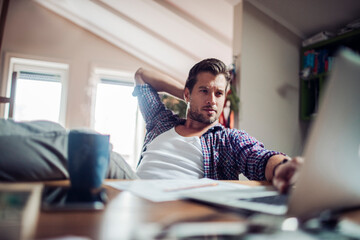 Obraz premium Young man working and using a laptop at home and having coffee