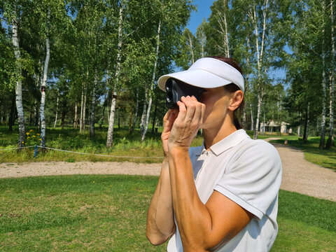 Woman golfer looks into rangefinder to measure distance