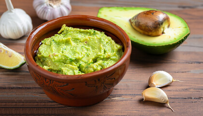 Clay bowl with fresh guacamole, lemon and garlic on wooden table. Diet vegetarian Mexican food avocado.