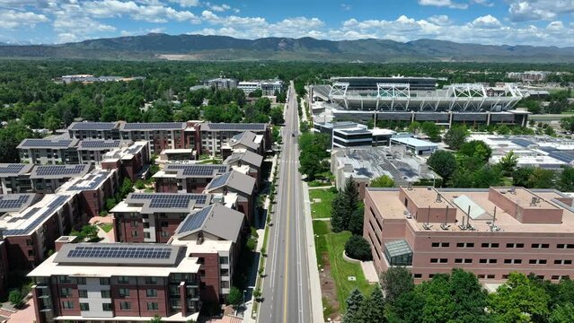 College campus dorms and apartments with solar panels on roofs with university stadium. Aerial shot of Colorado State University in Fort Collins with a mountain backdrop in summer.