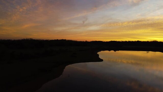 Rising from a dark shore the calm lake reflects the golden light of the sunset of Mechels Broek. 