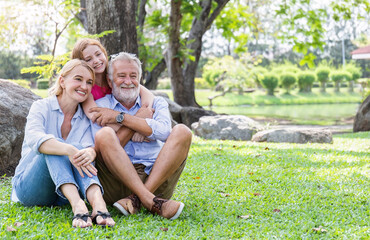 Fototapeta premium Portrait of happy family senior man woman and little girl relax in park. Mature elder family of three having fun together outdoor. Home school education, adopted child family lifestyle spring summer