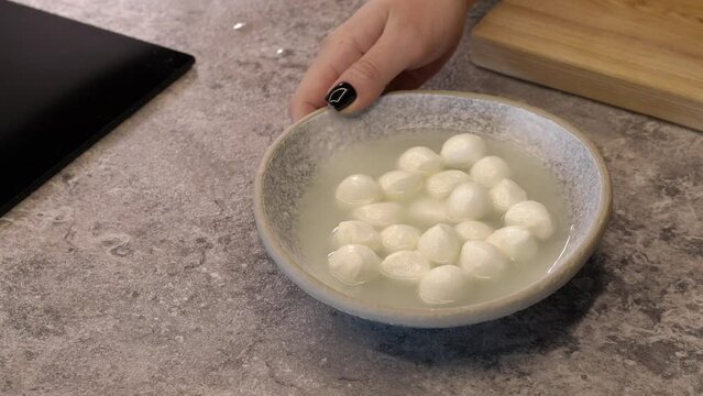 Balls of mozzarella cheese. A hand puts a plate of cheese on the table.