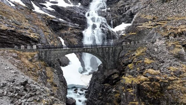 Stigfossen waterfall bridge along Trollstigen road fv 63 in Rauma Romsdal Norway - Rising aerial showing beautiful old stone bridge with waterfall and snow patches in background