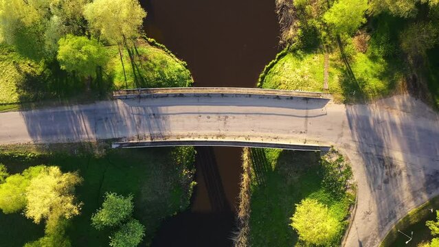 Top down rising view above concrete bridge spanning small quaint river in countryside