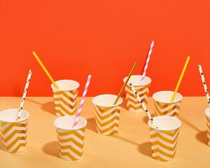A pattern of festive colored paper cups with straws with interesting designs on the table. Space for text. Theme of celebration and fun.