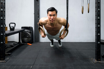 Athlete performing intense pull-up workout on gymnastic rings in a well-equipped, modern gym. The...