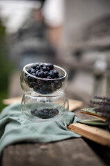 Autumn mood, blueberries in a glass cup on a wooden bench on a background of green grass, an open book and a green cloth napkin are nearby
