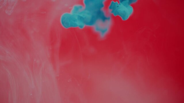Droplets of Blue Ink and Paint being Dropped into A Tank of Water on a Red Background.
