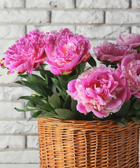 Beautiful peonies in wicker basket on white table near brick wall