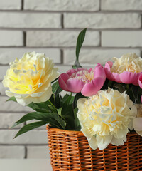 Beautiful peonies in wicker basket on white table near brick wall