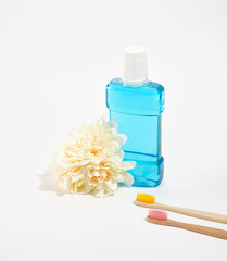 Blue mouthwash and organic bamboo toothbrushes with colorful bristles isolated. Fresh lush flower.