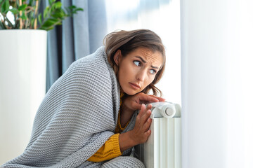 Unwell woman renter in blanket sit in cold living room hand on old radiator.suffer from lack of...
