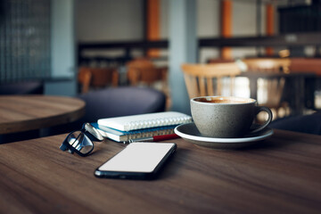 Coffee drink on table in cafe with mobile phone, eyeglasses and note books. people taking a break during a day with coffee drink in cafe