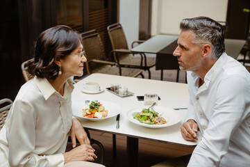 Mature man and woman having lunch in cafe outdoors