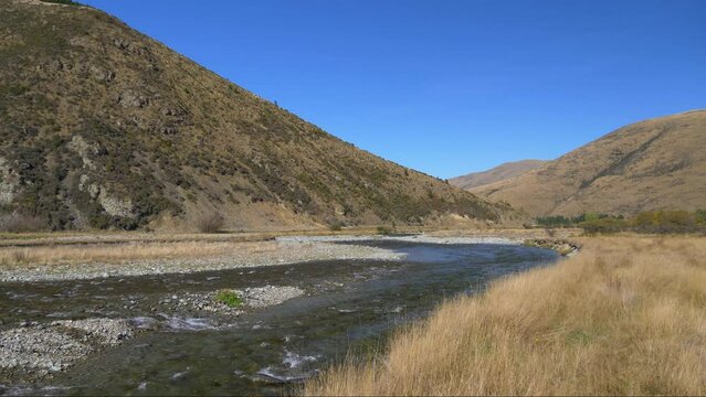 Panning shot of clear river flowing through hills and dry grassland