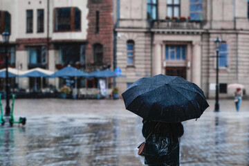 A woman with an umbrella in the rain walks along the street of the city. Bad weather.