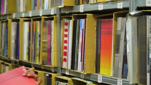 Vinyl discographies boxed and placed on shelves in order ready for restocking very organised numerically and alphabetised inside a warehouse that is a distributor for artists male grabbing an album