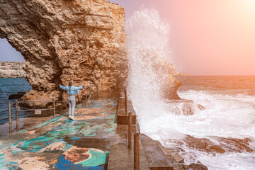 woman sea travel. A woman in a blue jacket stands on a rock above a cliff above the sea, looking at the stormy ocean. Girl traveler rests, thinks, dreams, enjoys nature