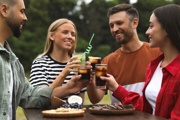 Happy friends clinking glasses with cocktails at table outdoors