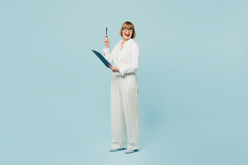 Full body employee business woman 50s wearing white classic suit glasses formal clothes clipboard with paper account documents point finger up isolated on plain blue background. Achievement concept.