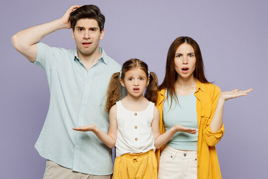 Young confused sad happy parents mom dad with child kid daughter girl 6 years old wearing blue yellow casual clothes look camera spread hands isolated on plain purple background. Family day concept.