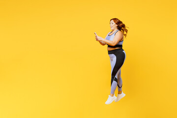 Fototapeta na wymiar Full body side view young chubby plus size big fat fit woman wear blue top warm up training use mobile cell phone jump high isolated on plain yellow background studio home gym. Workout sport concept.