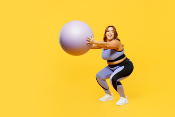 Full body sideways young chubby plus size big fat fit woman wear blue top warm up training hold in hands fit ball do squats isolated on plain yellow background studio home gym. Workout sport concept.