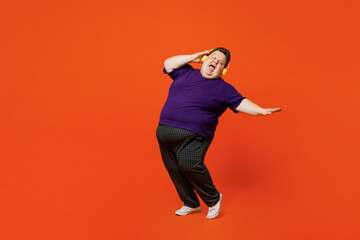 Fototapeta na wymiar Full size body young cheerful cool chubby overweight man wear purple t-shirt casual clothes listen to music in headphones dance sing have fun isolated on plain red orange background Lifestyle concept