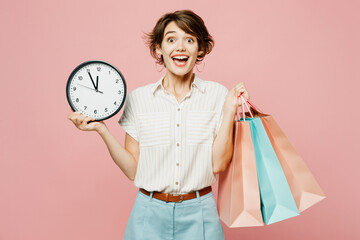 Young surprised woman wear casual clothes hold shopping paper package bags look camera hold in hand clock isolated on plain light pastel pink color background studio Black Friday sale buy day concept