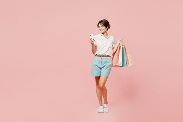Fototapeta na wymiar Full body young smiling woman wear casual clothes hold shopping paper package bags hold in hand use mobile cell phone isolated on plain pink color background studio. Black Friday sale buy day concept.