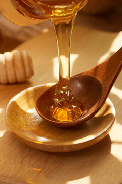 Tasty natural yellow golden bee honey flows in a thin stream from a spoon into a plate