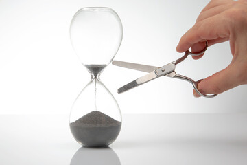 hand with scissors near the hourglass. time stop concept.