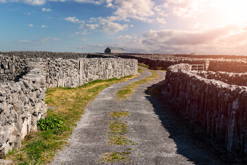 Small narrow road between stone fences with stunning nature scenery. Warm sunny day, cloudy sky. Aran island, county Galway, Ireland. Travel and tourism industry. Popular tourist attraction.