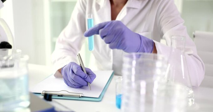 Scientist biologist writes research report and holds test tube with blue liquid. Method for assessing the toxicity of biological fluids