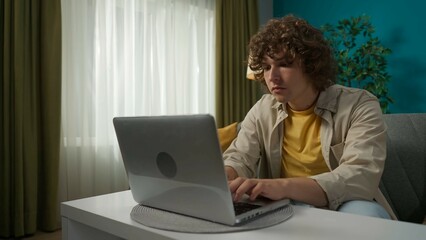 Young handsome man sitting on the sofa in the living room and working on his laptop with serious face