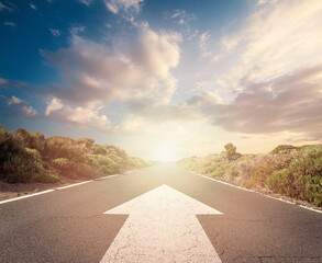 Success concept on an open road with white arrow at sunset sky clouds - obrazy, fototapety, plakaty