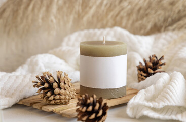 Fototapeta na wymiar Candle with blank label near pine cones and white sweater, Close up, copy space, mock up