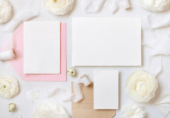 Obraz na płótnie Canvas Blank cards and envelopes near cream roses and white ribbons top view, wedding mockup