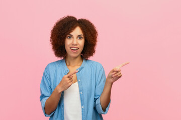 Happy excited African American woman pointing her finger at an empty space isolated on pink color background