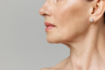 Cropped profile portrait with lips and chin neckline of middle-aged woman over grey studio...