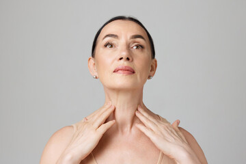 Double chin treatment. Elderly woman touching skin on neck over light grey background. Copy space...