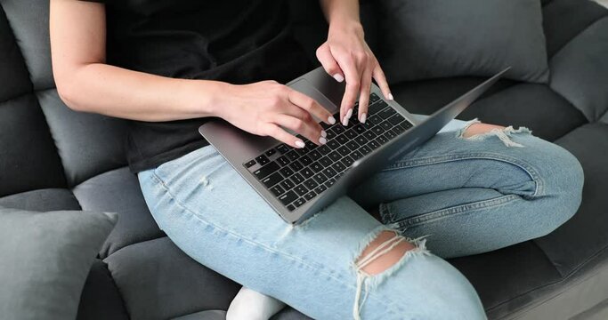 ands of a female laptop user sitting on sofa closeup. Freelance business woman working on computer at home